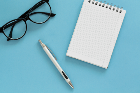 Symbolbild für Kurse speziell für Ältere: Brille, Stift und Notizblock auf hellblauem Hintergrund.