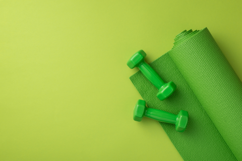 Symbolbild für den Programmbereich Gesundheit: Hanteln und eine Yogamatte vor grünem Hintergrund.